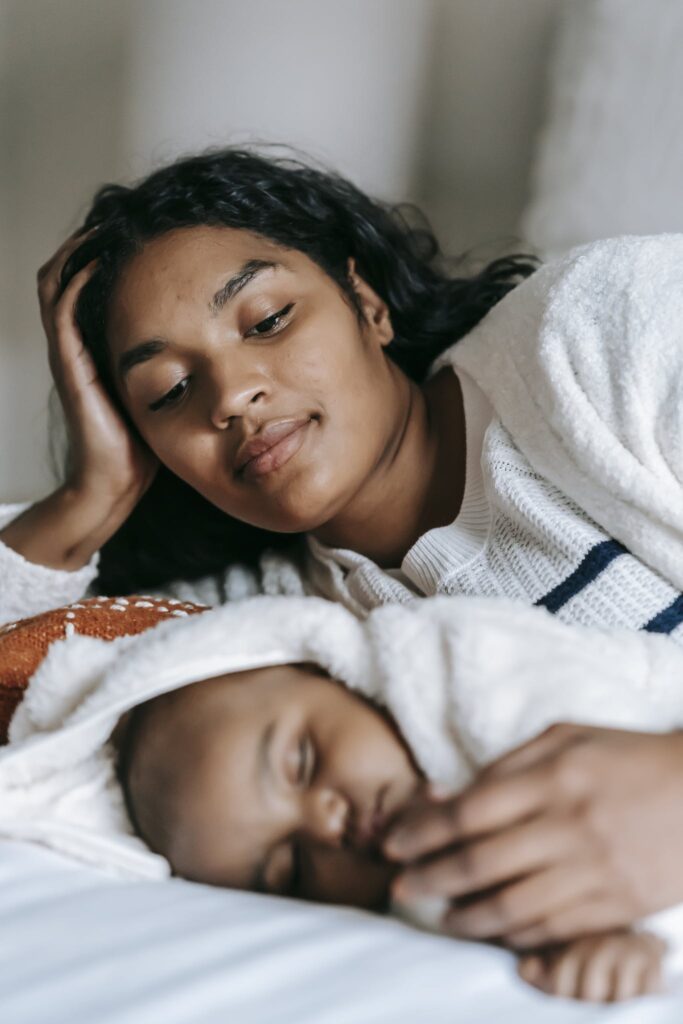 Loving ethnic mother embracing sleeping baby on bed