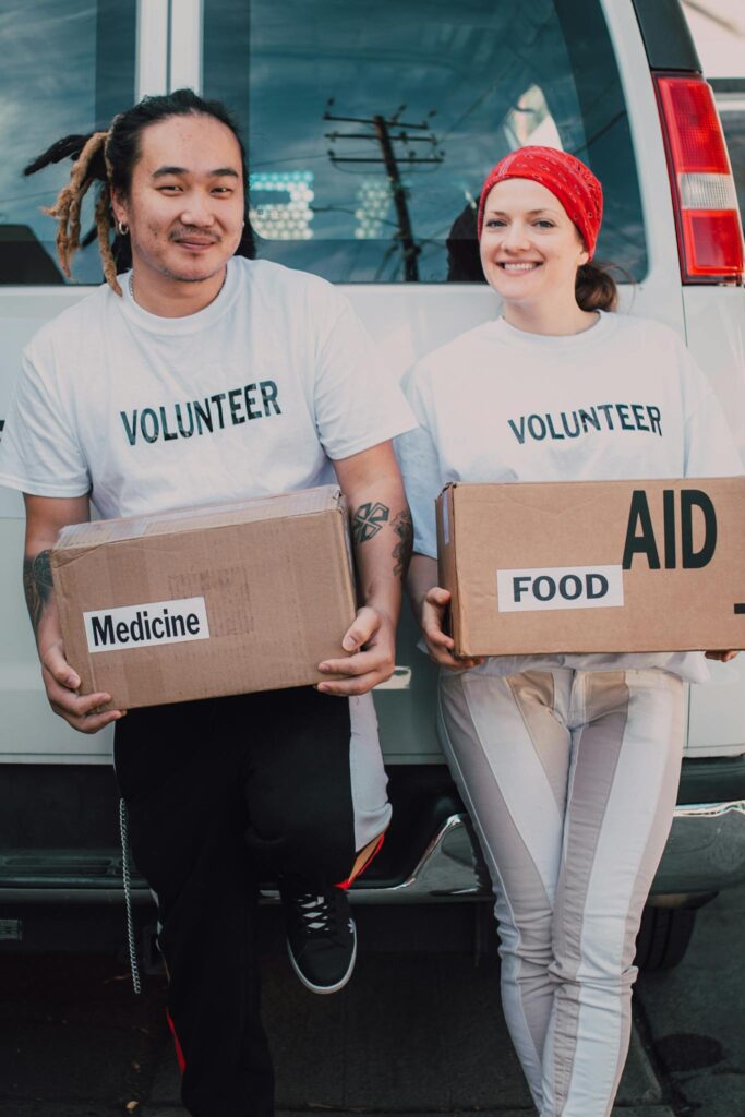 Man and Woman Carrying Medicine and Food Labelled Cardboard Boxes Behind a White Van